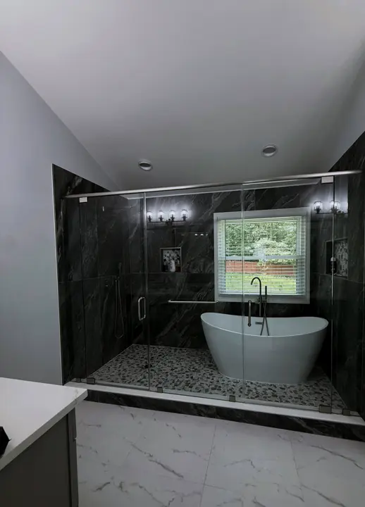 The same master bath after: a glass-enclosed wet room with charcoal stone tile and a freestanding tub