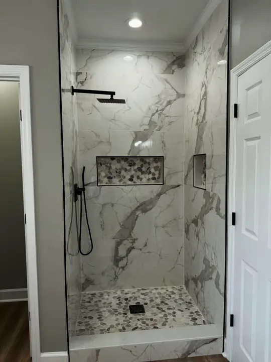 Walk-in shower with marble-look tile, black fixtures and a pebble floor
